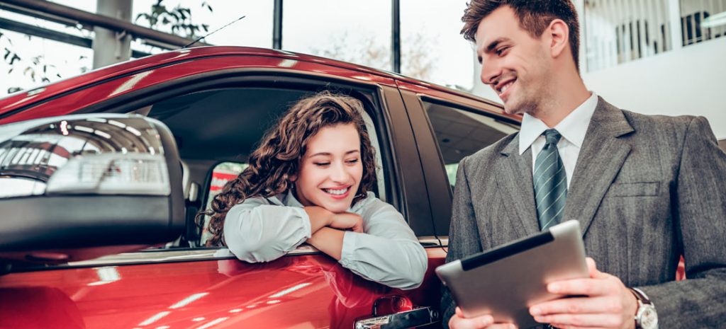 Clienta y vendedor en un concesionario digital, él sujeta una tablet donde muestra las ventajas del coche